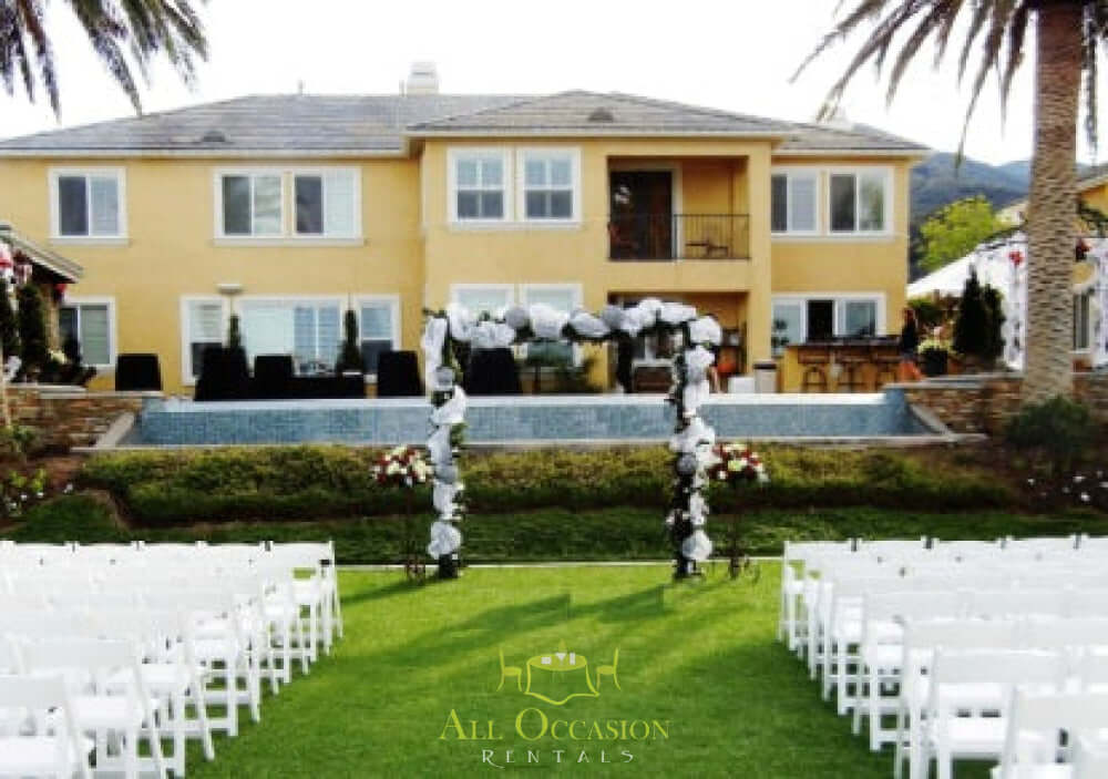 Iron Arch with Draping set up for a wedding ceremony, surrounded by floral arrangements and white chairs.