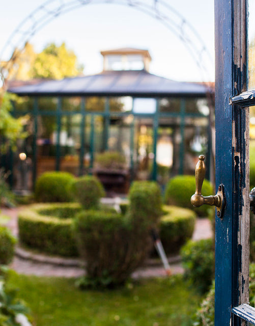 View through an open door to a well-kept garden with a glasshouse and trimmed hedges.