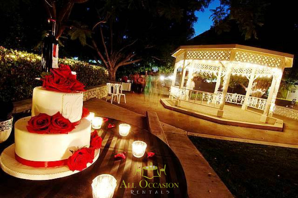 Elegant wedding cake with red roses in outdoor event setting, featuring rental gazebo and table decor, ideal for Corona event rentals.