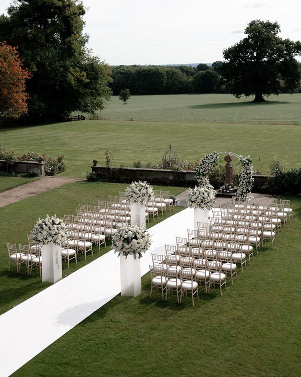 Outdoor ceremony with white aisle and floral pillars for elegant weddings
