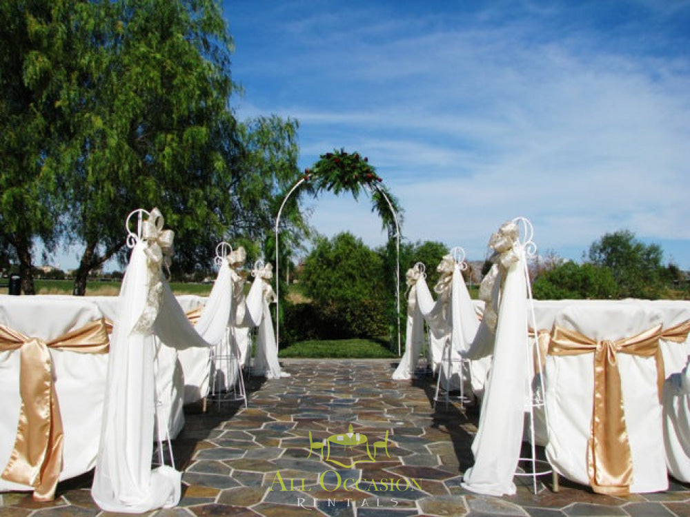 Iron white arch set for a wedding ceremony with draping and decorated chairs, ideal for Corona event rentals.