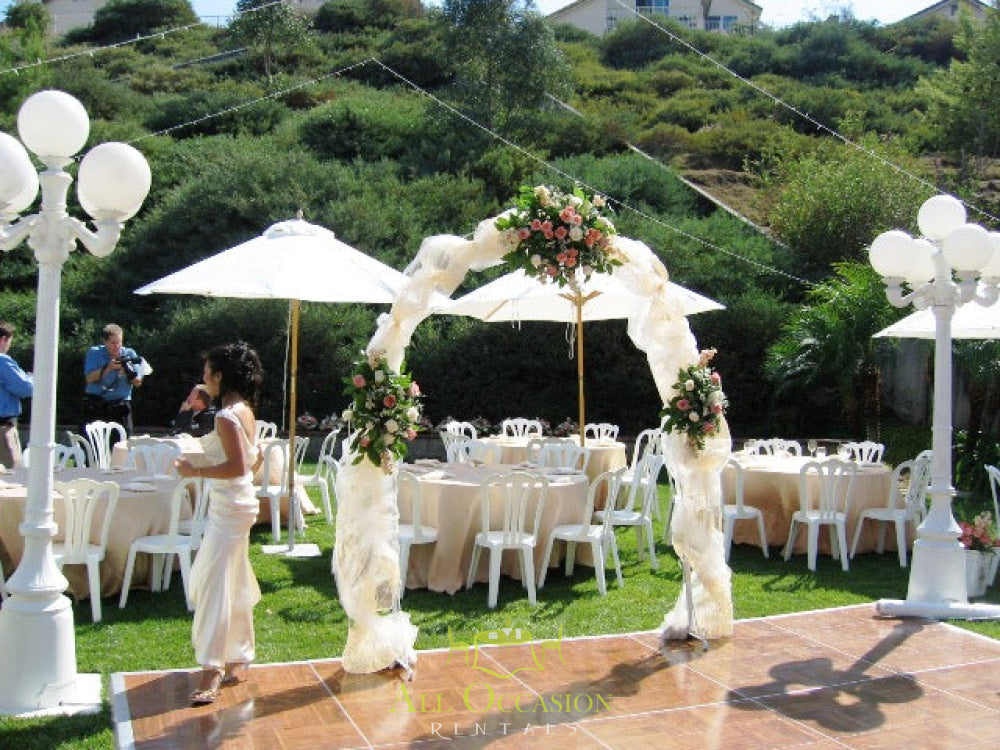 Elegant white iron arch at an outdoor wedding setup with banquet tables and chairs, ideal for event rentals in Corona.
